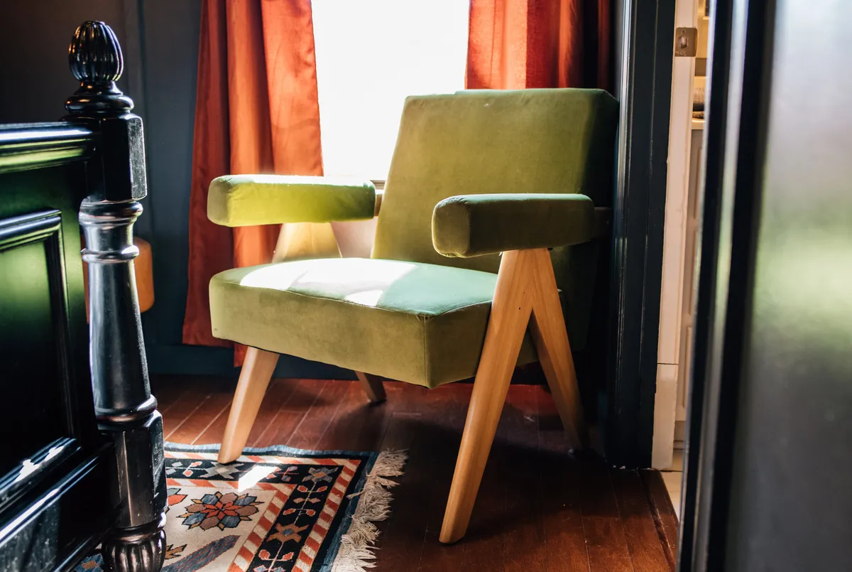 A chic corner featuring a lush green velvet chair, bold orange curtains, and a decorative rug, all bathed in cozy light. The setting suggests a versatile spot for reading, relaxing, or socializing, contributing to the studio's flexible atmosphere.