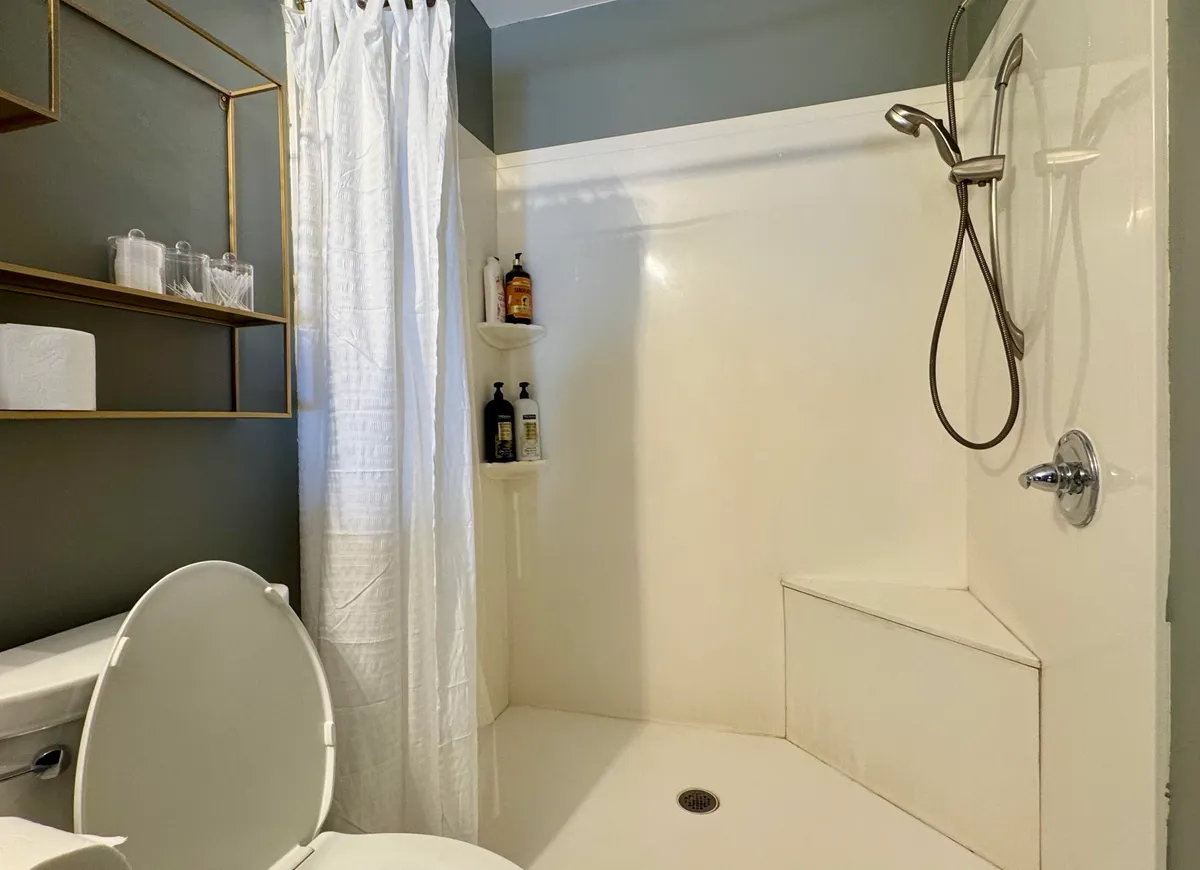 A tranquil bathroom scene featuring a walk-in shower, neatly arranged toiletries on a shelf, and plush towels. The soft lighting and uncluttered design evoke a soothing, spa-like atmosphere ideal for relaxation after a busy day.