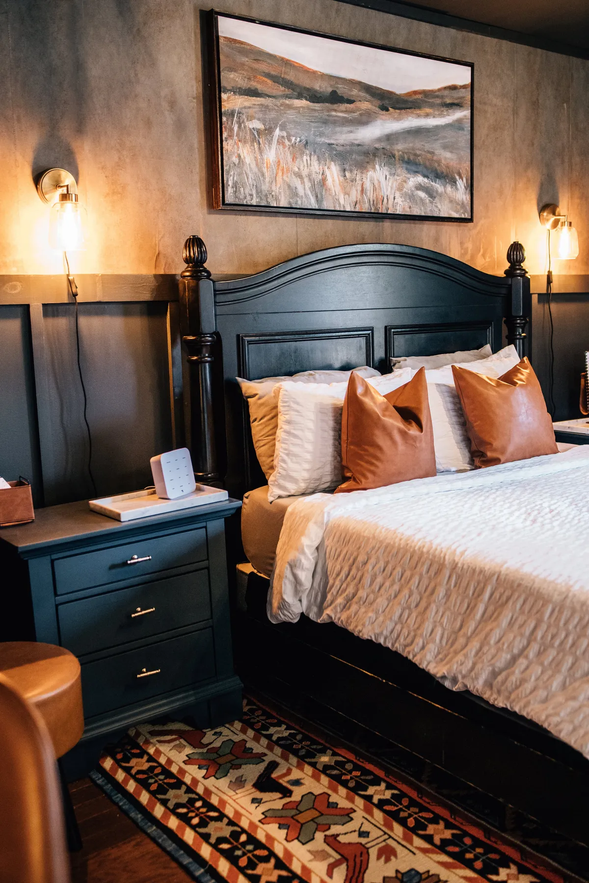 A cozy sleeping area with an inviting bed topped with plush pillows, tasteful artwork above the headboard, and a nightstand with soft lighting. The design balances intimacy and modern aesthetics, creating a restful retreat.